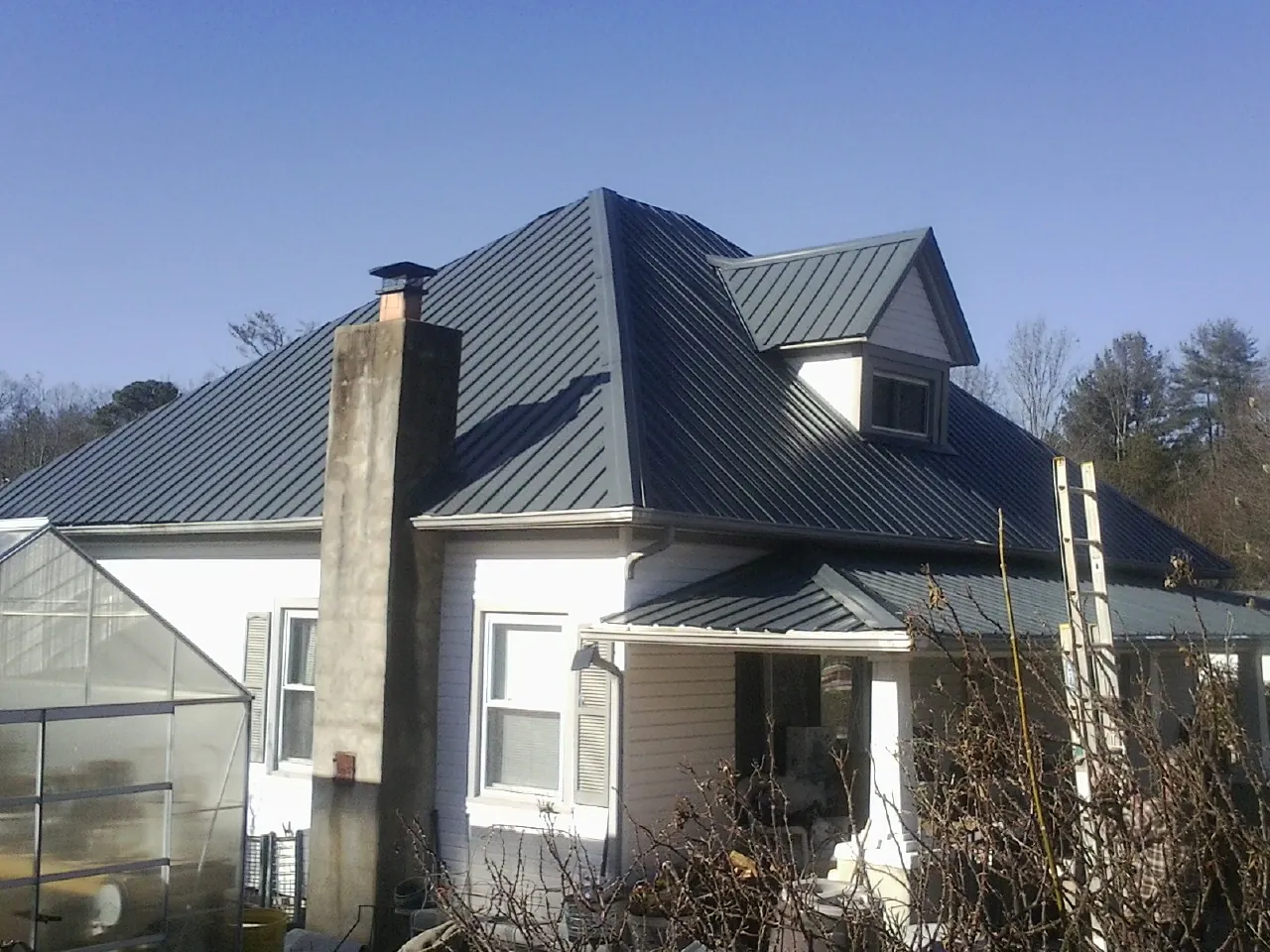 Dark blue standing seam metal roof on a white farmhouse with dormer — Slate & Tile Roof Repair by Roofing Brothers in Sugar City