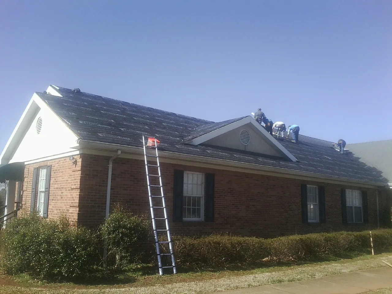 Crew tearing shingles off a brick ranch roof with a ladder set — Emergency Roof Repair work by our crew in Sugar City